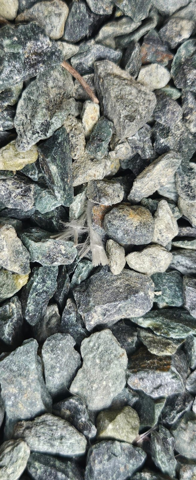 Green-grey angular pieces of crushed serpentinite gravel forming a car-park surface, photographed from above and filling the frame.